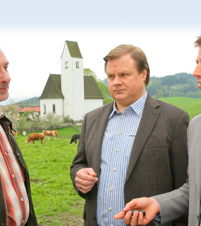 "Die Rosenheim-Cops - Sprung in den Tod": Auf einer Kuhweide an einer Kirche befragen die Ermittler Hansen (Igor Jeftic) und Hartl (Michael A. Grimm) Tierarzt Sendlinger (Daniel Friedrich).