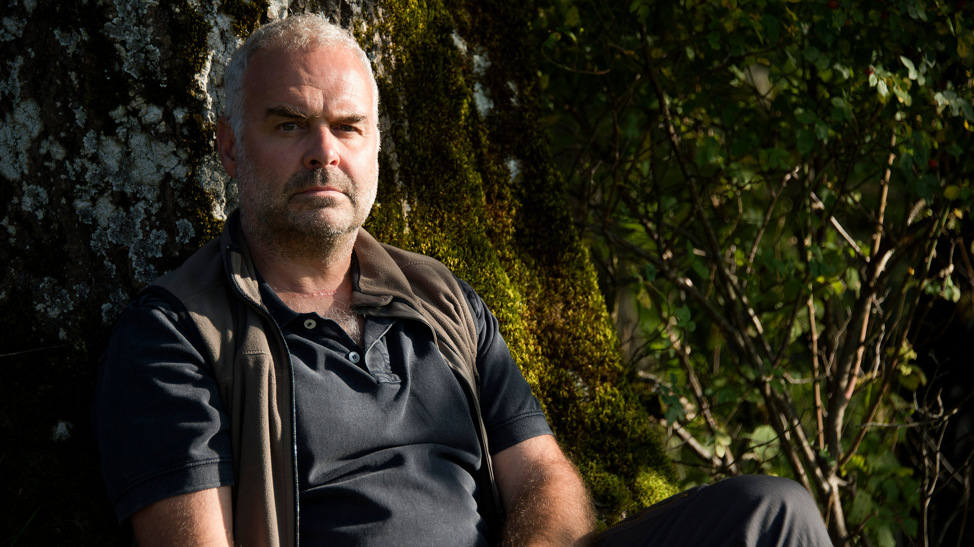 "Der Bergdoktor - Der bessere Tod (1)": Rolf Bichler (Jophi Ries) sitzt in Nahaufnahme vor einem Baum und schaut sorgenvoll in die Weite.