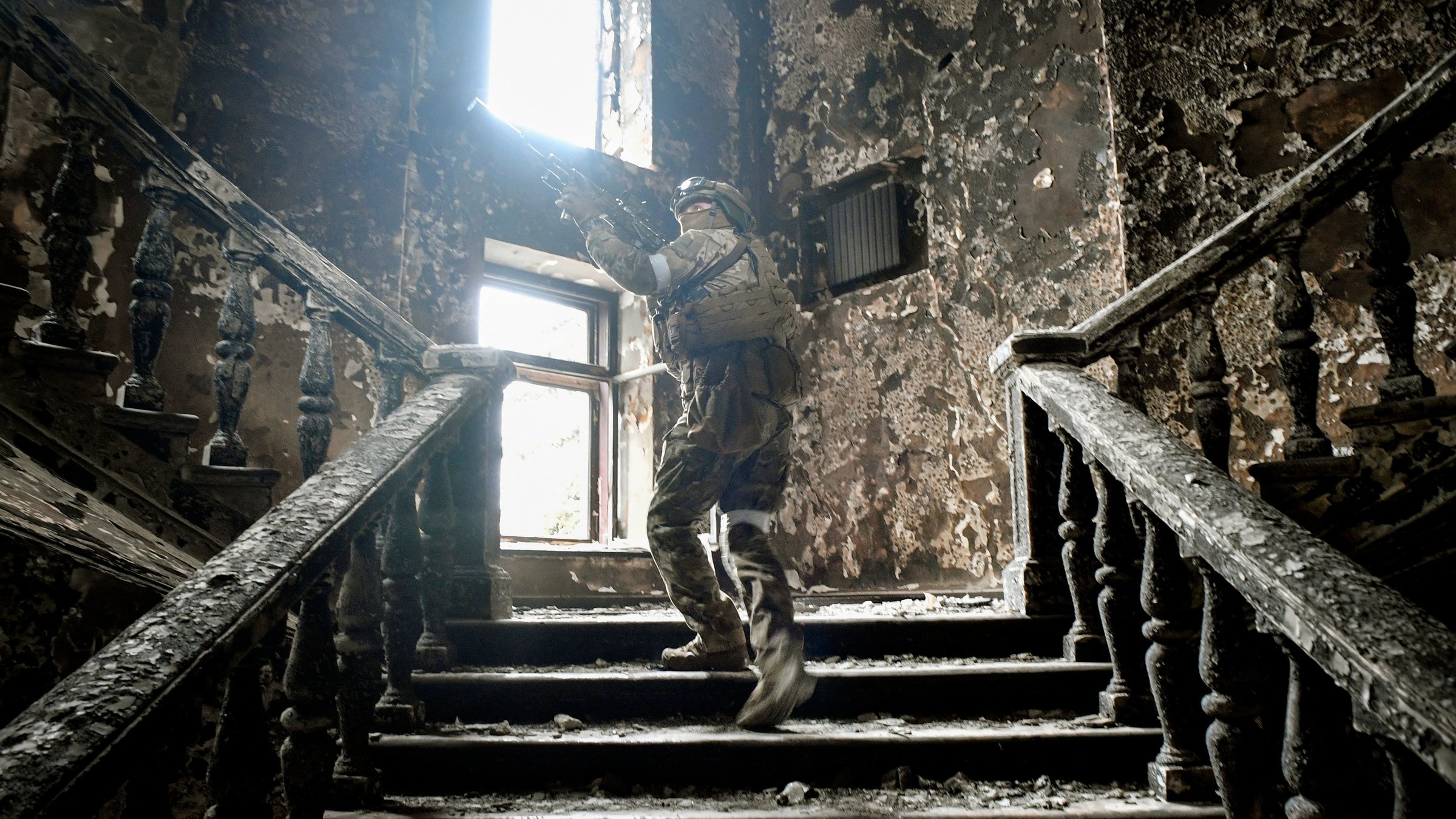 "Tatort Ukraine - Die Russen": Ein russischer Soldat geht mit Maschinengewehr im Anschlag eine Treppe im zerstörten Theater von Mariupol hoch.
