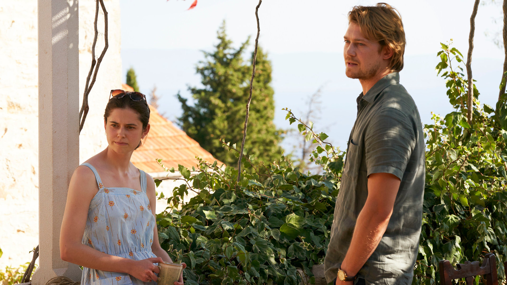 "Conversations with Friends - Am Siedepunkt": Frances (Alison Oliver) und Nick (Joe Alwyn) stehen sich vor einem blühenden Garten gegenüber und schauen aufmerksam zur Seite.