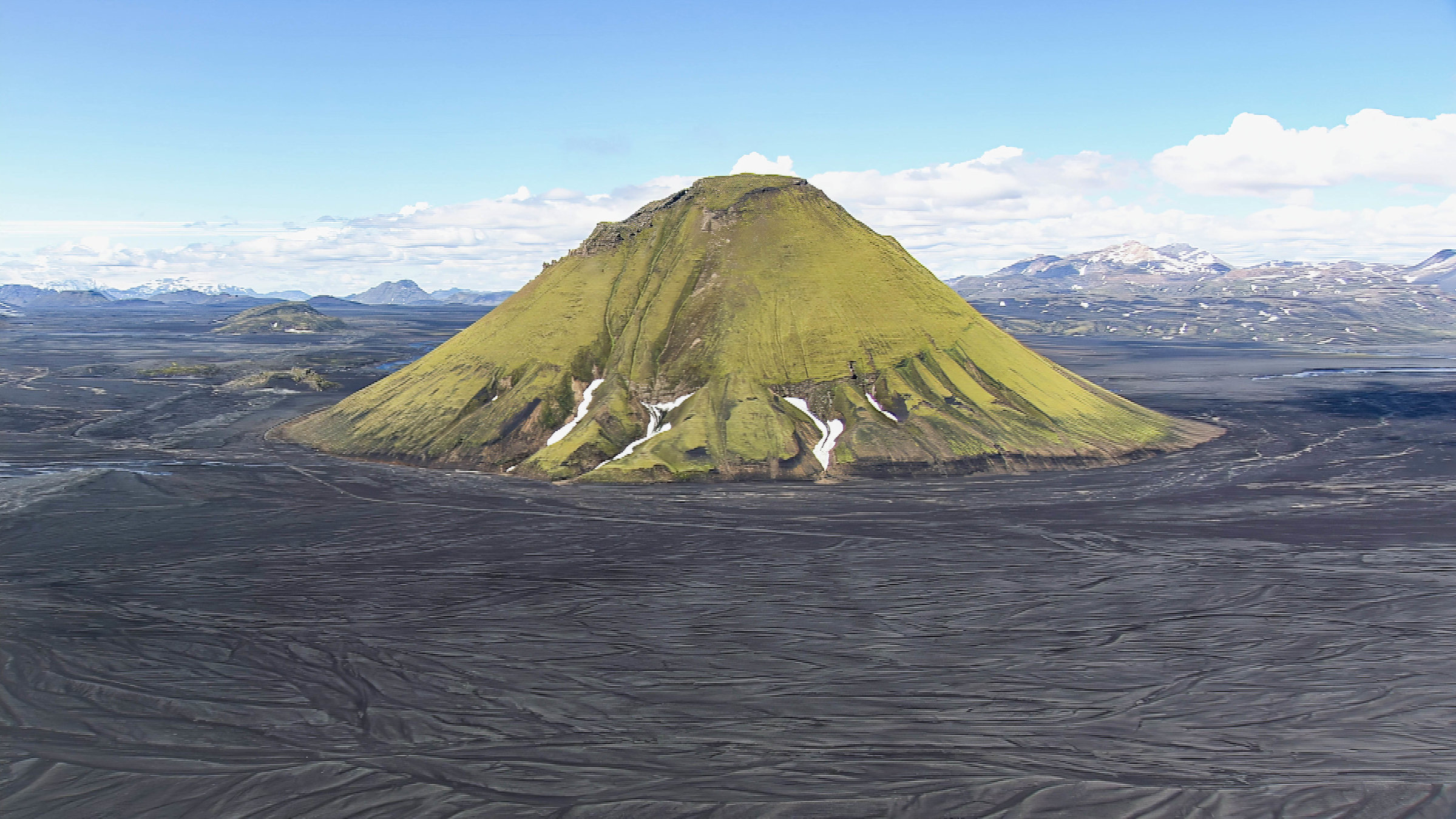 "Im Flug über Island": Ein kegelförmiger, grüner Berg, umgeben von dunkler Landschaft.