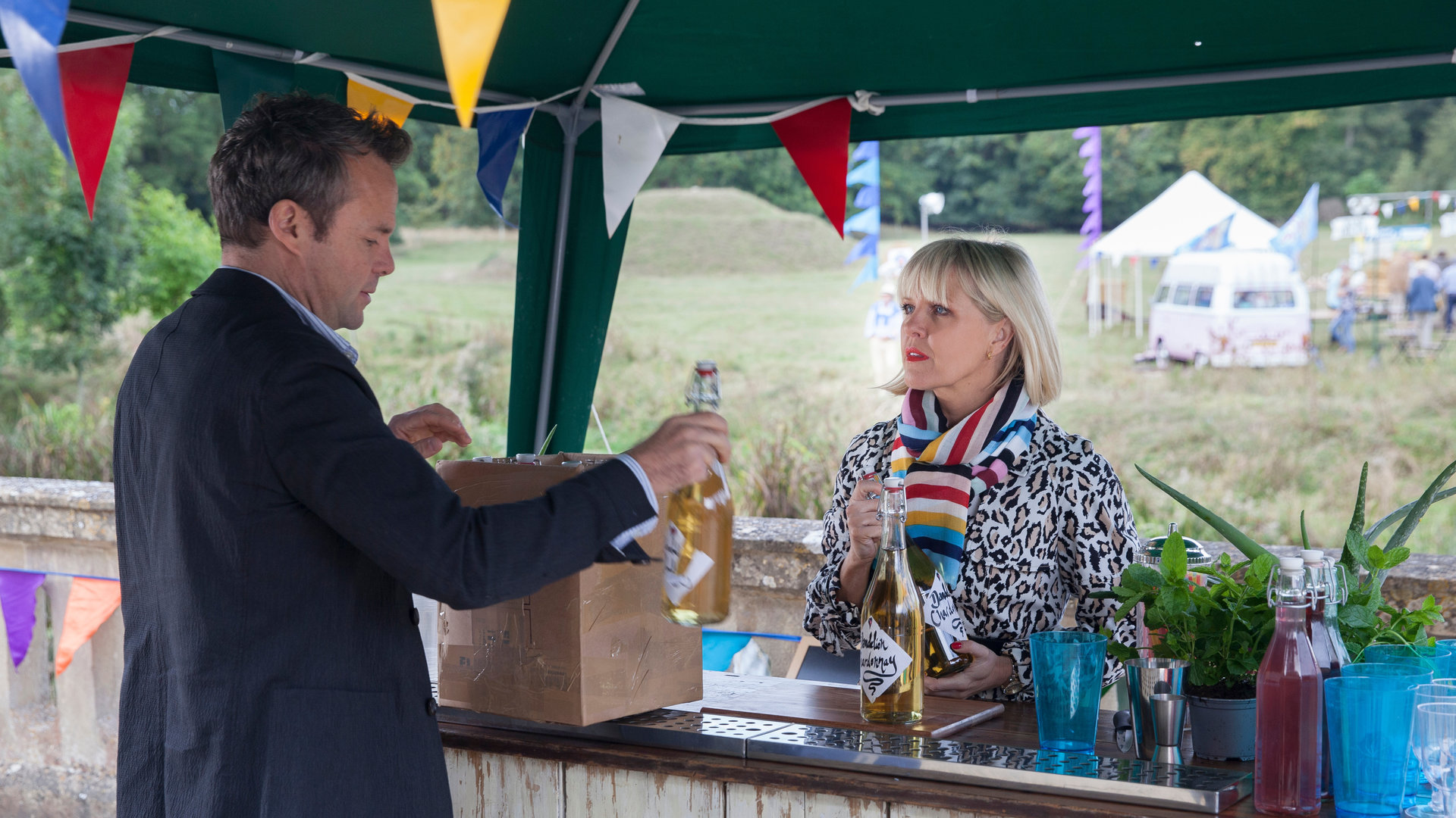 "Agatha Raisin - Der tote Kaplan Teil 2": Agatha Raisin (Ashley Jensen) steht an einer Bar und blickt zu James Lacey (Jamie Glover).