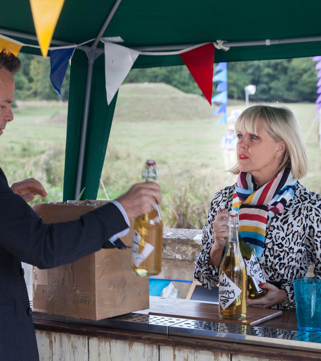"Agatha Raisin - Der tote Kaplan Teil 2": Agatha Raisin (Ashley Jensen) steht an einer Bar und blickt zu James Lacey (Jamie Glover).