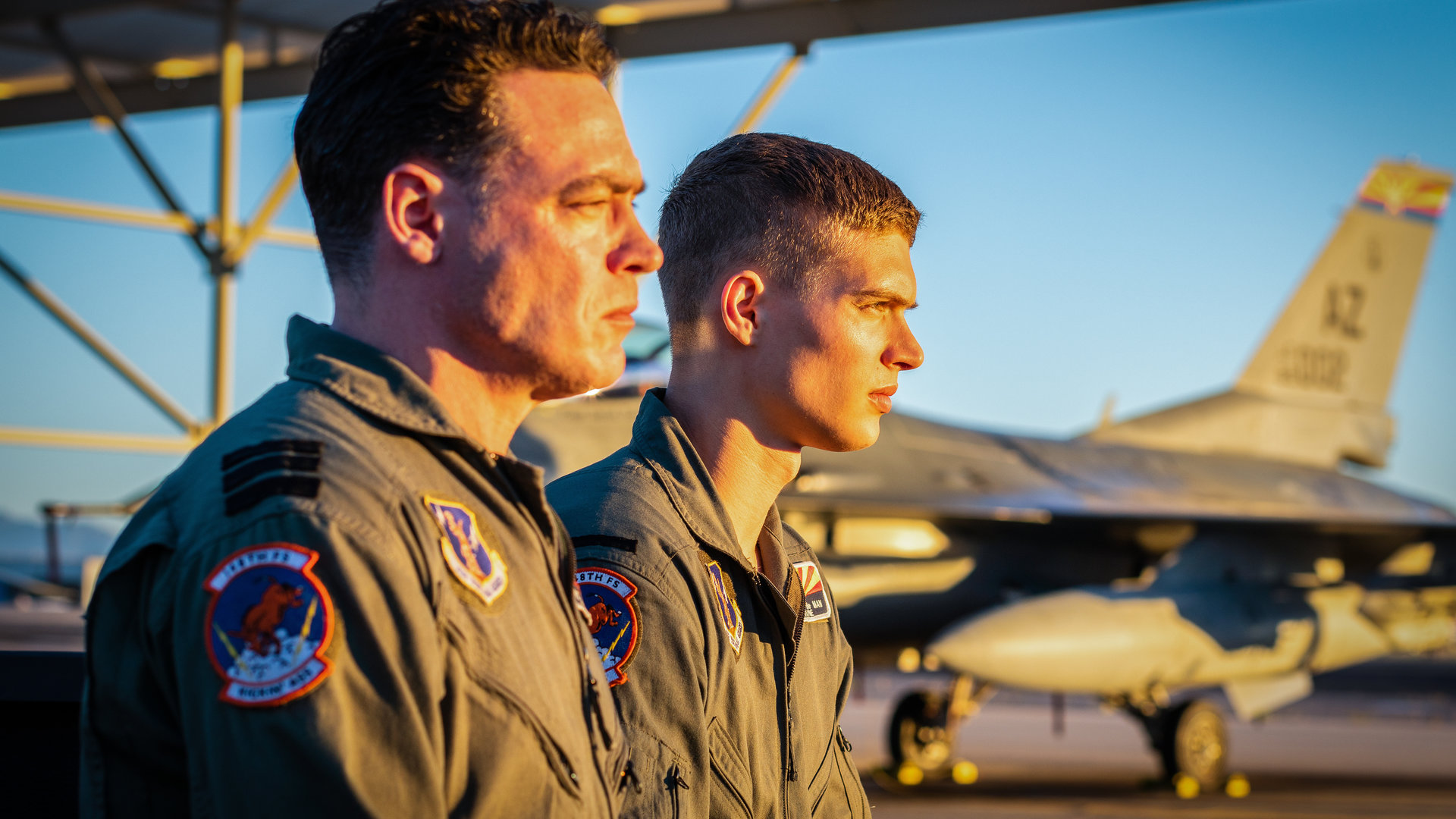 "High-Flyers - Sprich es aus": Ausbilder Derek "Lucky" Lanshof (Fedja van Huêt) und Rutger de Man (Josha Stradowski) sitzen nebeneinander auf dem Flugplatz in Tucson, Arizona. Im Hintergrund steht eine F-16.