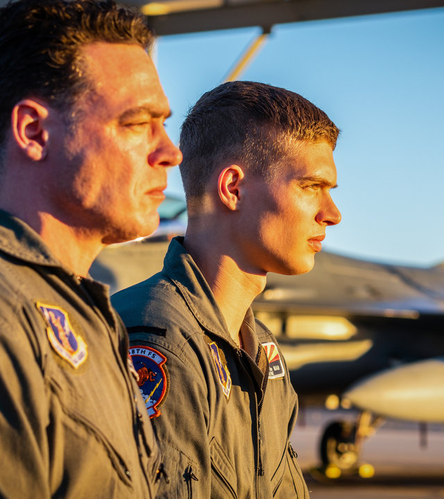 "High-Flyers - Sprich es aus": Ausbilder Derek "Lucky" Lanshof (Fedja van Huêt) und Rutger de Man (Josha Stradowski) sitzen nebeneinander auf dem Flugplatz in Tucson, Arizona. Im Hintergrund steht eine F-16.