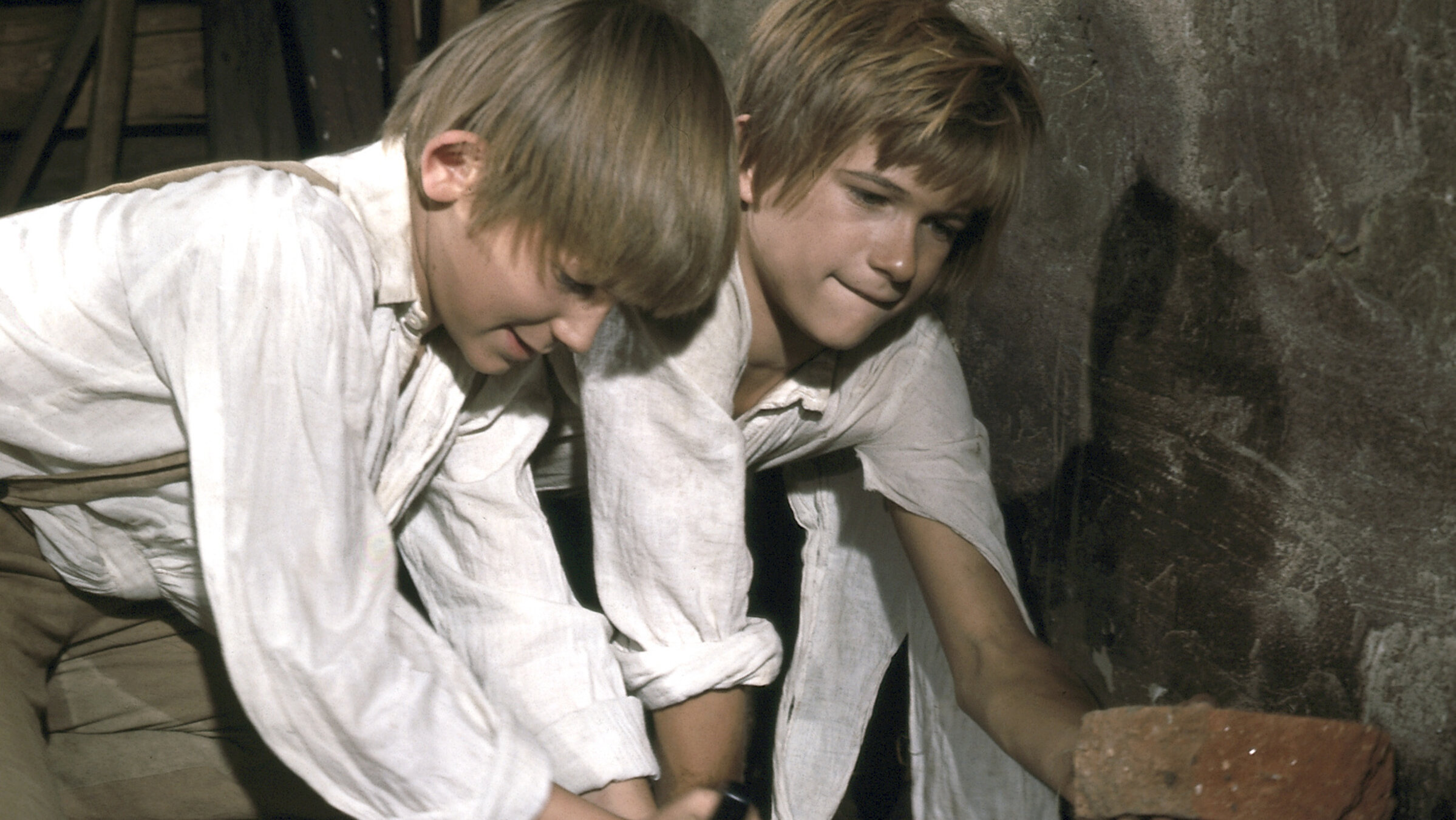 "Tom Sawyers und Huckleberry Finns Abenteuer - 2. Teil": Tom (Roland Demongeot) und Huck (Marc di Napoli) wühlen kniend in einem Raum den Boden auf.