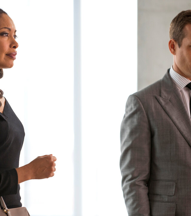 "Suits - Schwachstelle": Jessica (Gina Torres) und Harvey (Gabriel Macht) stehen nebeneinander in einem modernen, hell ausgeleuchteten Büro, beide blicken ernst in dieselbe Richtung.