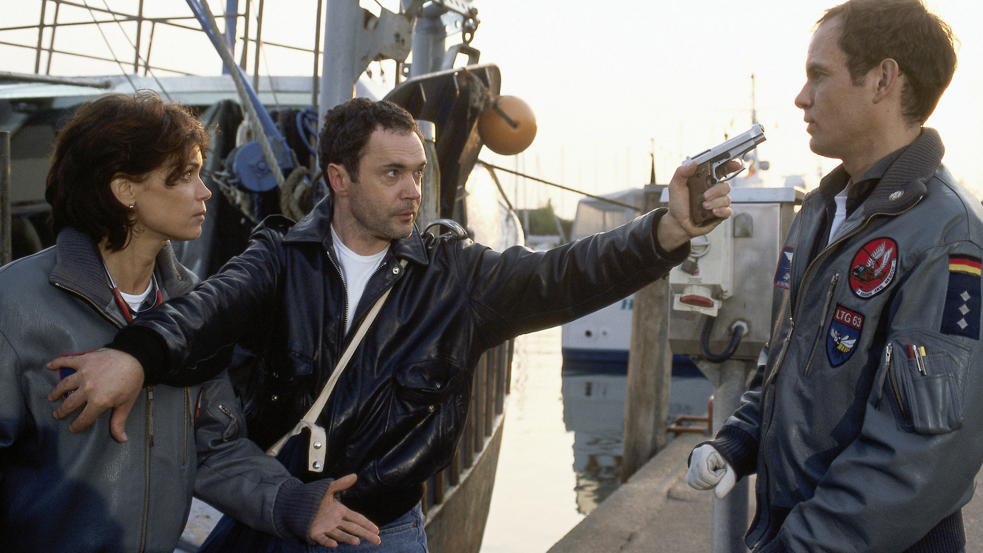"Die Rettungsflieger - Das Team in Not": Alex (Matthias Leja) und Maren (Gerit Kling) werden am Hafen von Joscha (Rainer Laupichler) mit einer Waffe bedroht.