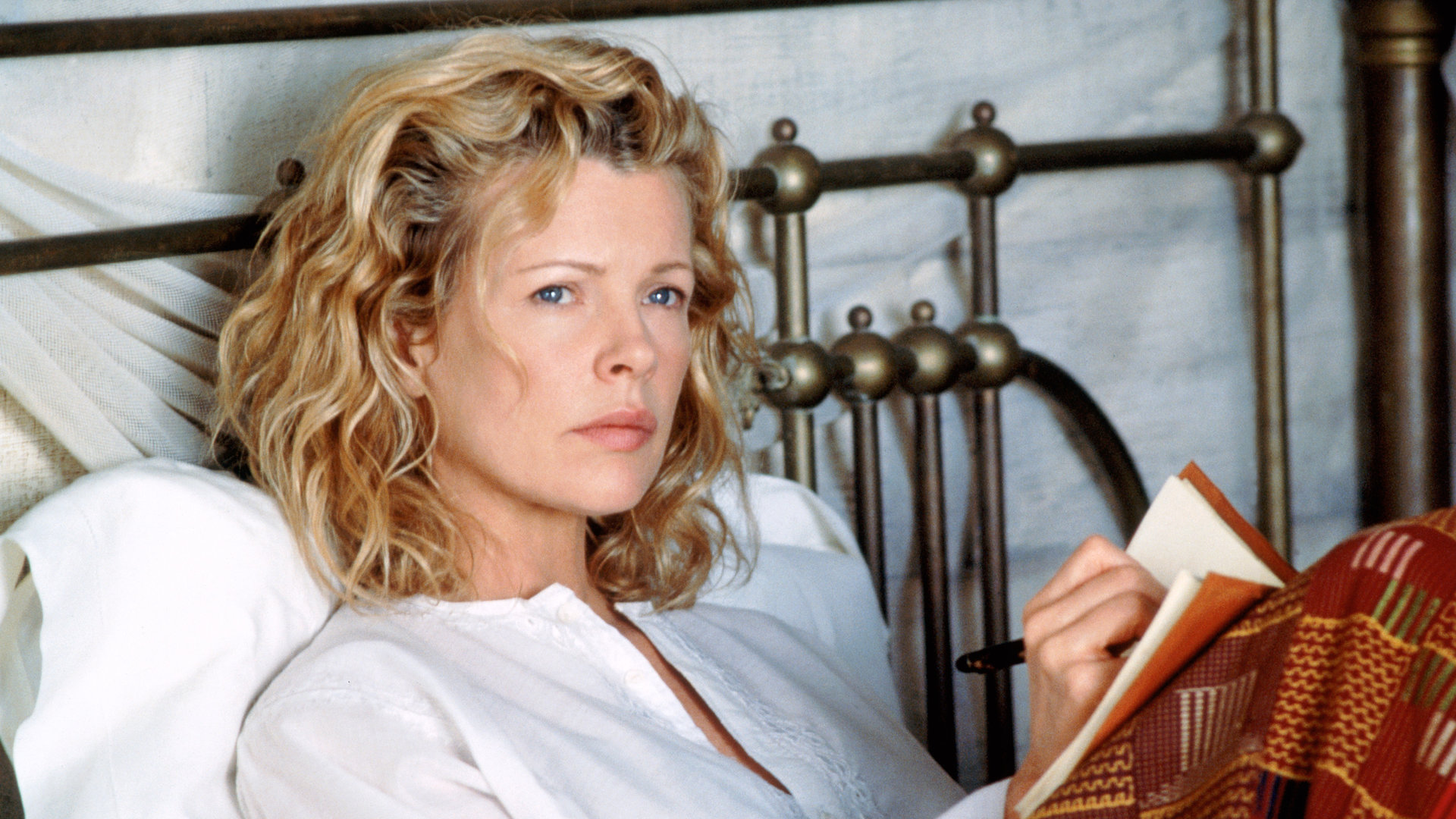 "Ich träumte von Afrika": Kuki Gallmann (Kim Basinger) sitzt im Bett mit einem Notizbuch auf den Knien und blickt nachdenklich in die Ferne.