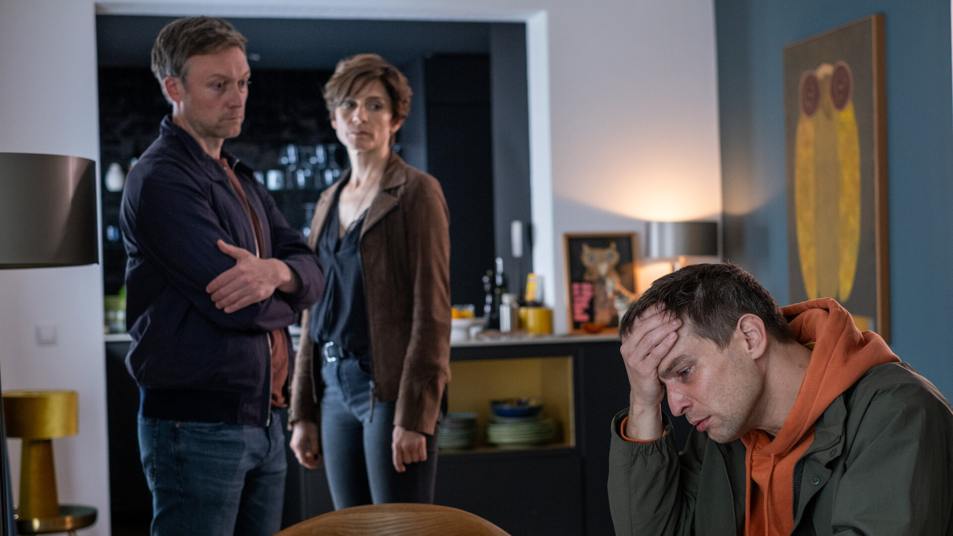 "In Wahrheit - Für immer Dein": In einem Wohnraum: Moritz Brück (Robert Finster) sitzt an einem Tisch und stützt seinen Kopf mit der Hand. Er blickt bedrückt nach unten. Im Hintergrund stehen Freddy Breyer (Robin Sondermann) und Judith Mohn (Christina Hecke) und schauen besorgt zu ihm.