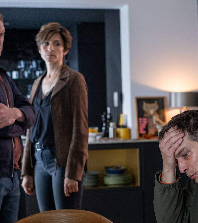 "In Wahrheit - Für immer Dein": In einem Wohnraum: Moritz Brück (Robert Finster) sitzt an einem Tisch und stützt seinen Kopf mit der Hand. Er blickt bedrückt nach unten. Im Hintergrund stehen Freddy Breyer (Robin Sondermann) und Judith Mohn (Christina Hecke) und schauen besorgt zu ihm.