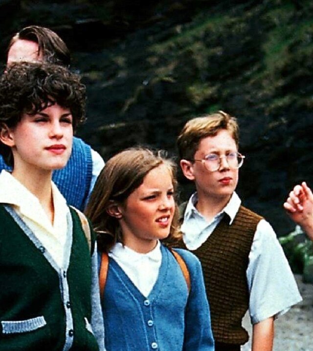 "Fünf Freunde verfolgen die Strandräuber": Julian (Marco Williamson), George (Jemima Rooper), Anne (Laura Petela), ein Junge und Dick (Paul Child) stehen nebeneinander vor einer steilen Felswand. Die Kinder schauen alle in eine Richtung.