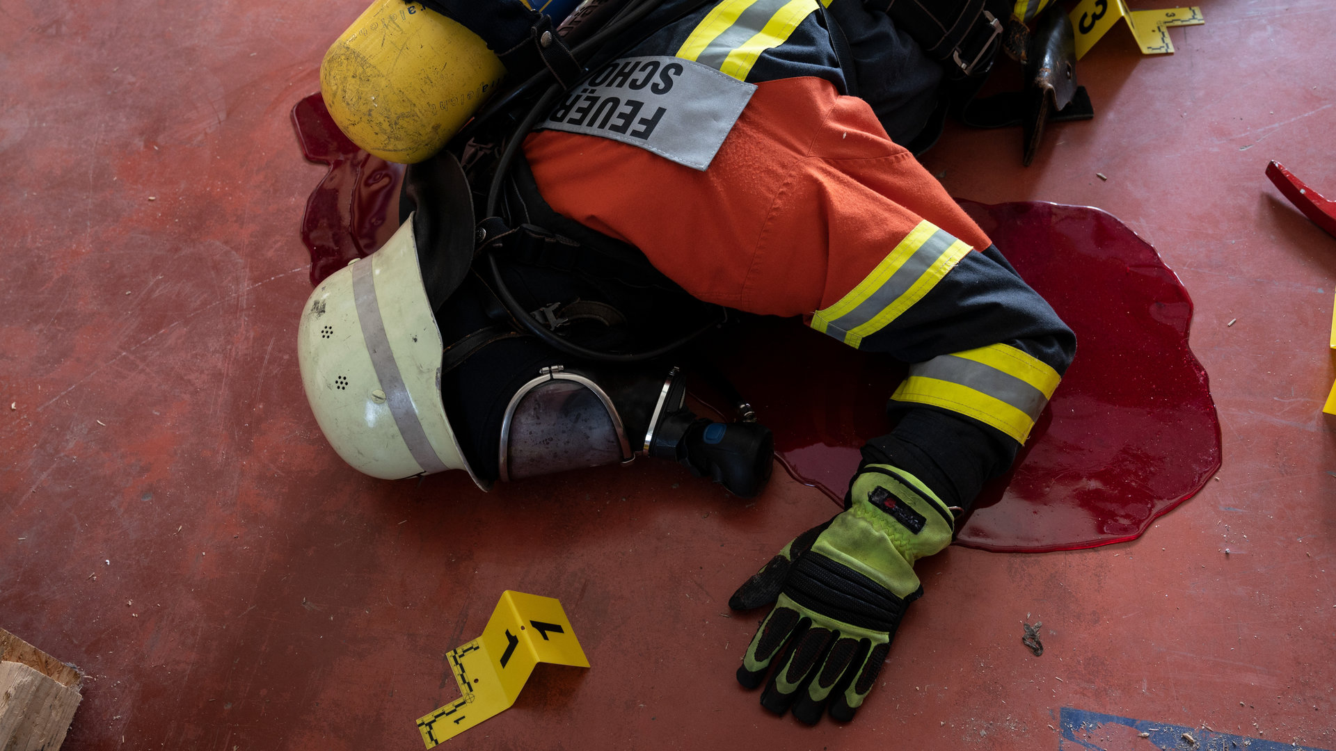 “SOKO Stuttgart – Unsichtbare Gefahr“: Ein Feuerwehrmann liegt in voller Einsatzmontur und mit Gasmaske erschlagen auf dem Boden. Unter seinem leblosen Körper ist eine große Blutlache zu sehen. Neben der Leiche wurden bereits Tatortnummerntafeln der Spurensicherung aufgestellt.