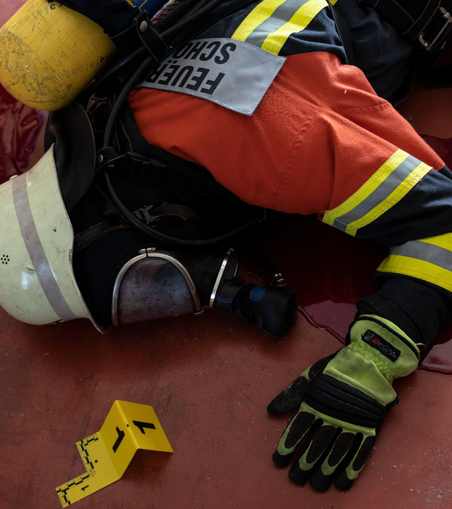 “SOKO Stuttgart – Unsichtbare Gefahr“: Ein Feuerwehrmann liegt in voller Einsatzmontur und mit Gasmaske erschlagen auf dem Boden. Unter seinem leblosen Körper ist eine große Blutlache zu sehen. Neben der Leiche wurden bereits Tatortnummerntafeln der Spurensicherung aufgestellt.