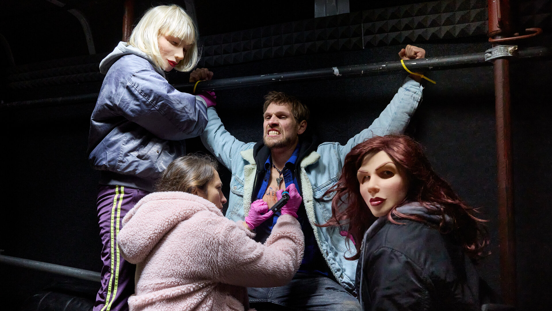 "Stralsund – Ablaufdatum": Der gefesselte Jonathan Theisen (Remo Schulze) wird gegen seinen Willen von zwei Frauen, Nina (Cheyenne Demont) und Anja (Anna Herrmann), festgehalten, die Masken tragen und nicht zu identifizieren sind. Martha (Lo Rivera) kniet vor ihm, hat sein Hemd geöffnet und ist dabei ihn zu tätowieren.