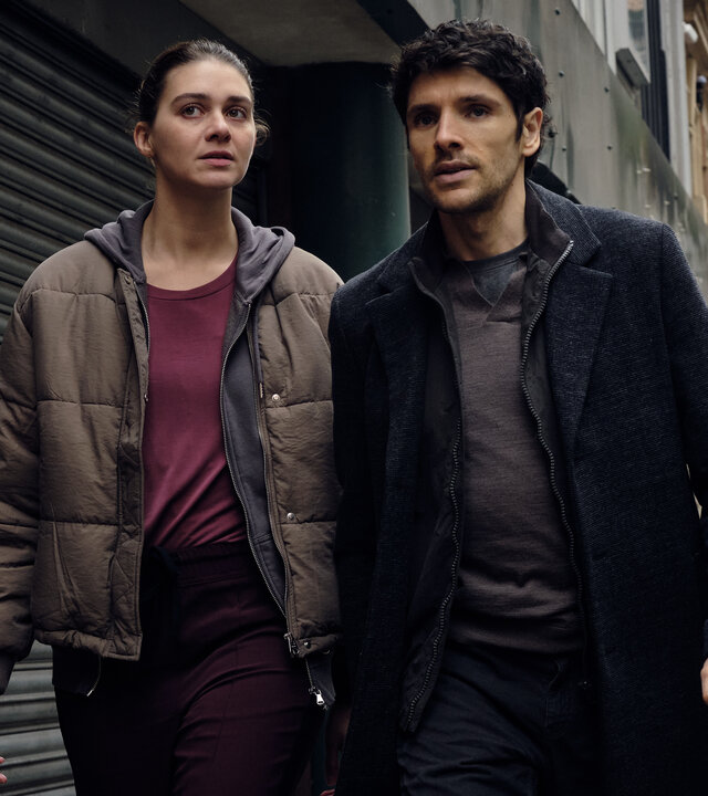 "The Killing Kind: Alles auf Anfang": John Webster (Colin Morgan) und Ingrid Lewis (Emma Appleton) gehen eng nebeneinander mit entschlossenem Blick eine Straße entlang.