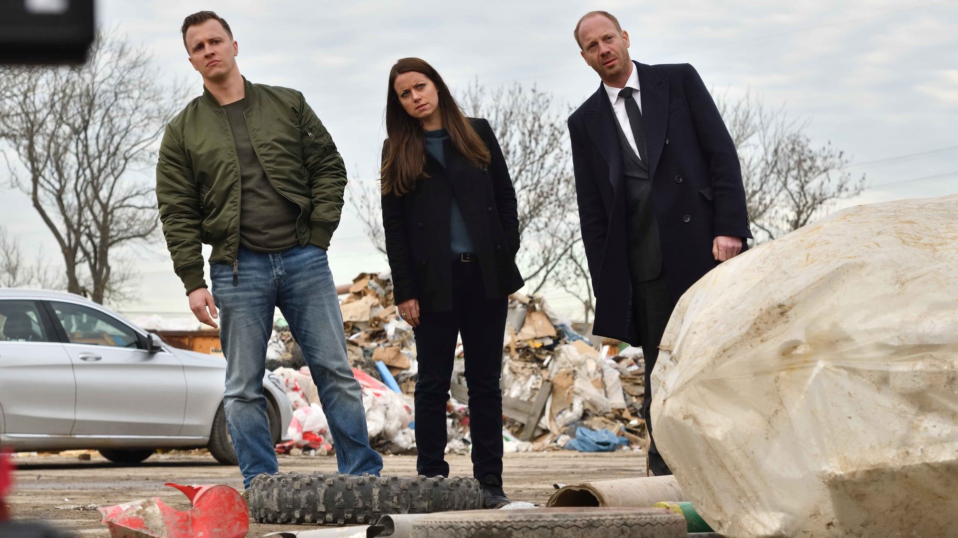 "Herr und Frau Bulle – Abfall": Yvonne (Alice Dwyer), Heiko (Johann von Bülow), und Kevin (Tim Kalkhof) stehen in einer Reihe auf einer Mülldeponie und neigen sich alle nach links.