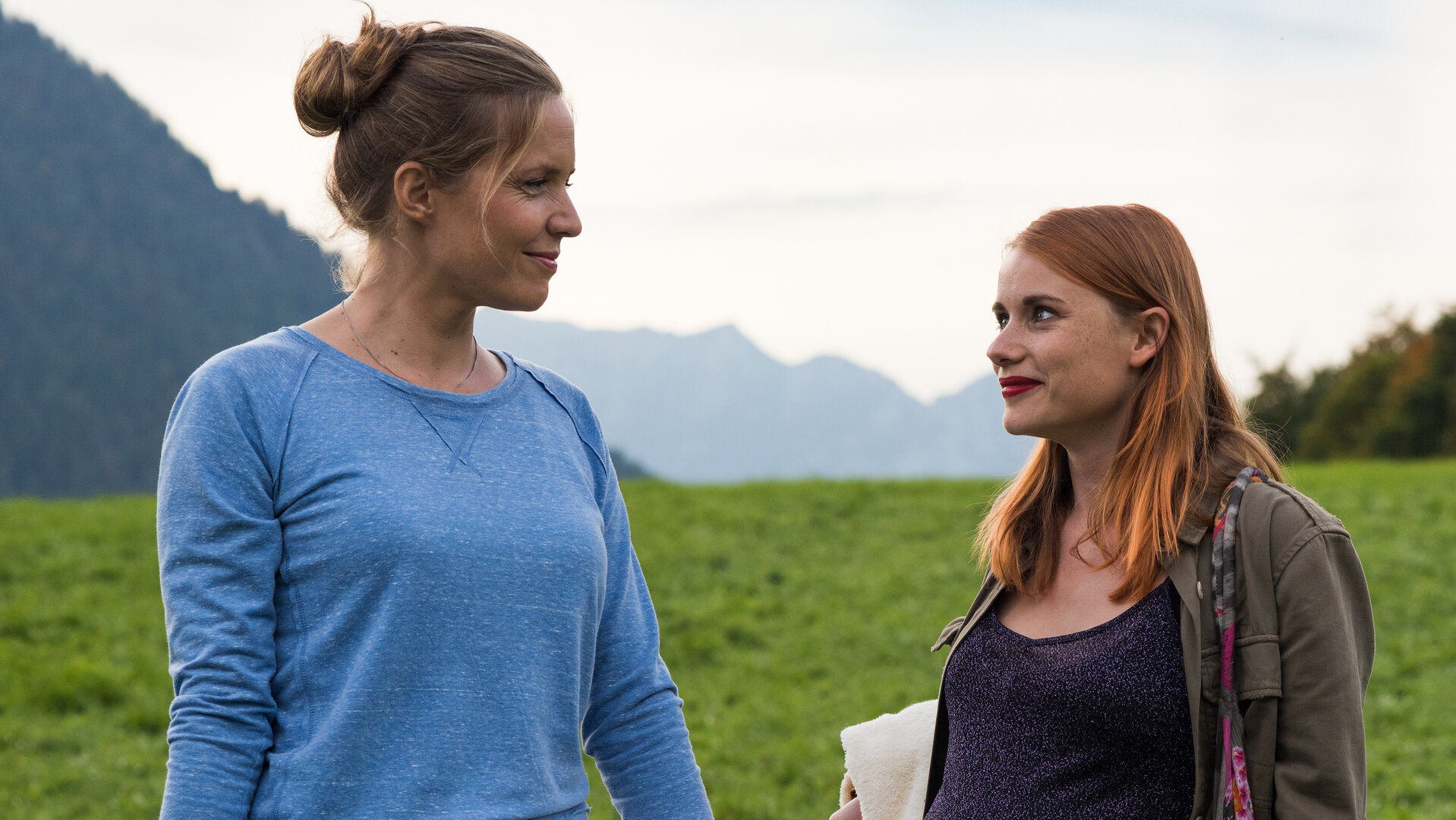 "Lena Lorenz - Zwei Väter": Auf einer Wiese vor Bergpanorama stehen Lena Lorenz (Patricia Aulitzky) und Anna König (Anna Hausburg) und unterhalten sich.