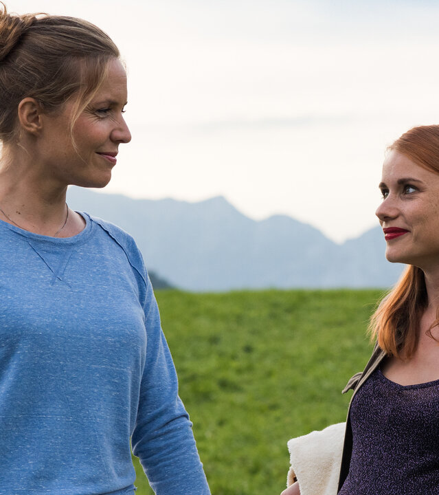 "Lena Lorenz - Zwei Väter": Auf einer Wiese vor Bergpanorama stehen Lena Lorenz (Patricia Aulitzky) und Anna König (Anna Hausburg) und unterhalten sich.