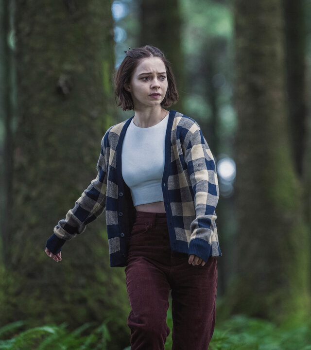 "A Good Girl's Guide to Murder – Eine unglaublich dumme Idee": Pip (Emma Myers) rennt scheinbar orientierungslos durch einen dichten Wald. Sie trägt eine karierte Stoffjacke über einem weißen Top und schaut hilflos, als suche sie jemanden.