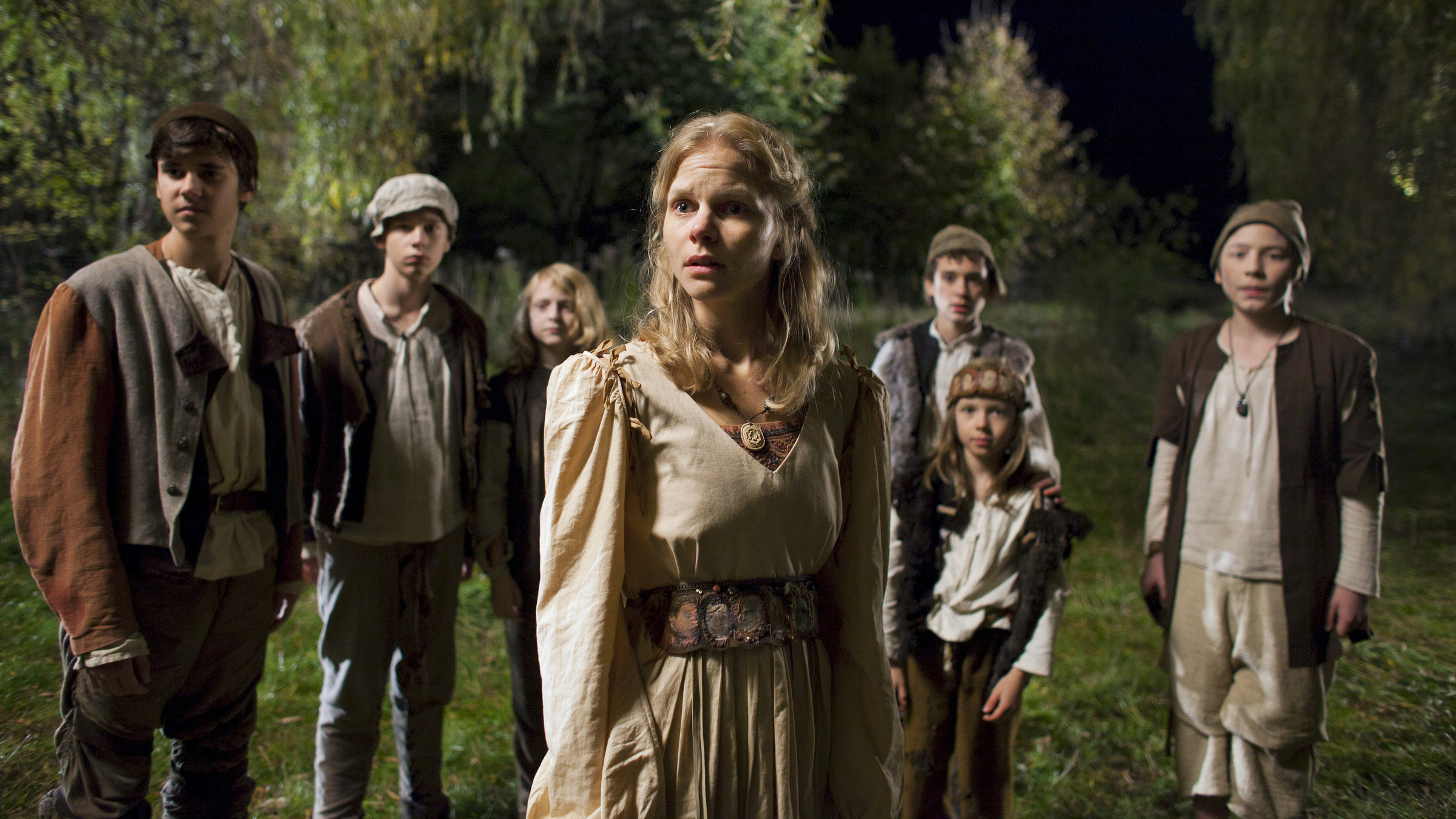 "Die sechs Schwäne": In den Kleidern von Bauernkindern stehen in der Dunkelheit im Halbkreis die sechs Brüder, in ihrer Mitte Constanze (Sinja Dieks). Alle schauen in die gleiche Richtung.