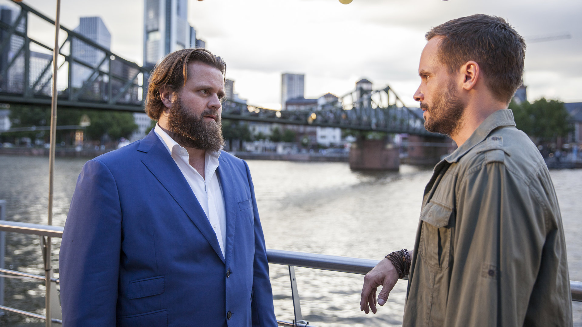 "Ein Fall für zwei - Gemeinsam einsam": Benni (Antoine Monot, Jr.) und Leo (Wanja Mues) stehen sich auf einem Hausboot gegenüber. Im Hintergrund ist die Frankfurter Skyline zu erkennen.