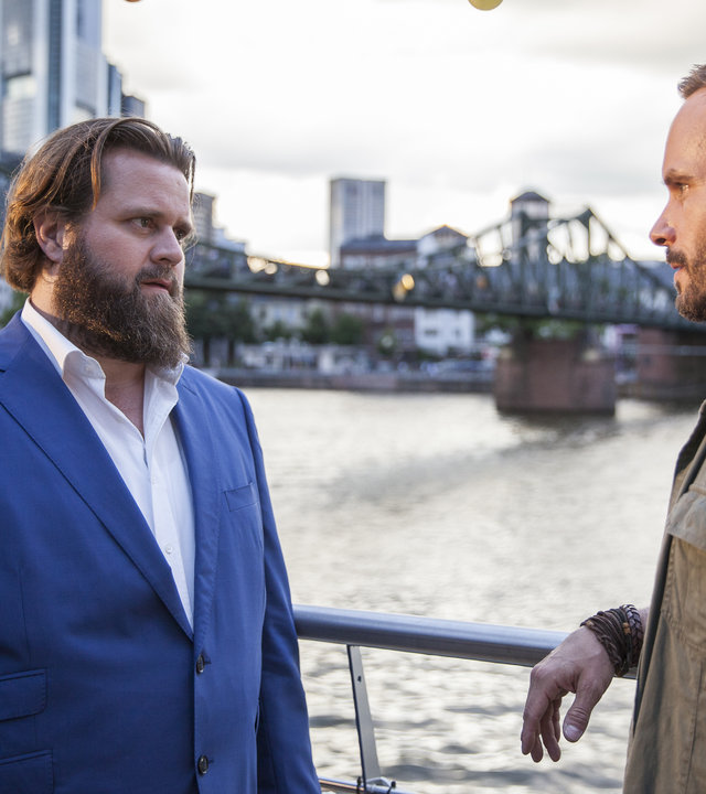 "Ein Fall für zwei - Gemeinsam einsam": Benni (Antoine Monot, Jr.) und Leo (Wanja Mues) stehen sich auf einem Hausboot gegenüber. Im Hintergrund ist die Frankfurter Skyline zu erkennen.