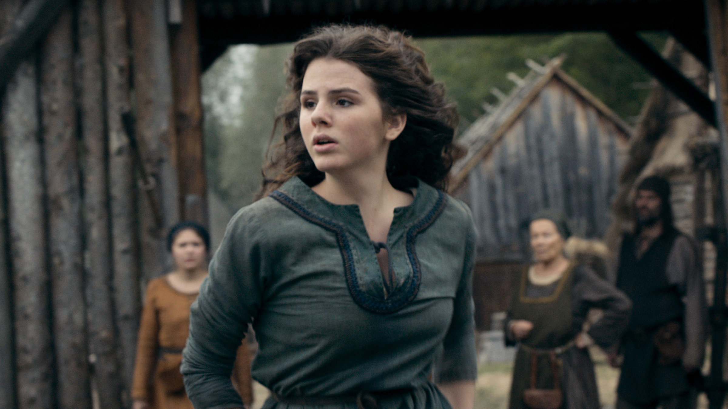 "Das Geheimnis der Hebamme": Die junge Heilerin und Hebamme Marthe (Ruby O. Fee) schaut erschrocken auf etwas, das man nicht sieht. Im Hintergrund Holzhäuser und drei mittelalterlich gekleidete Dorfbewohner, die das Geschehen ebenfalls beobachten.