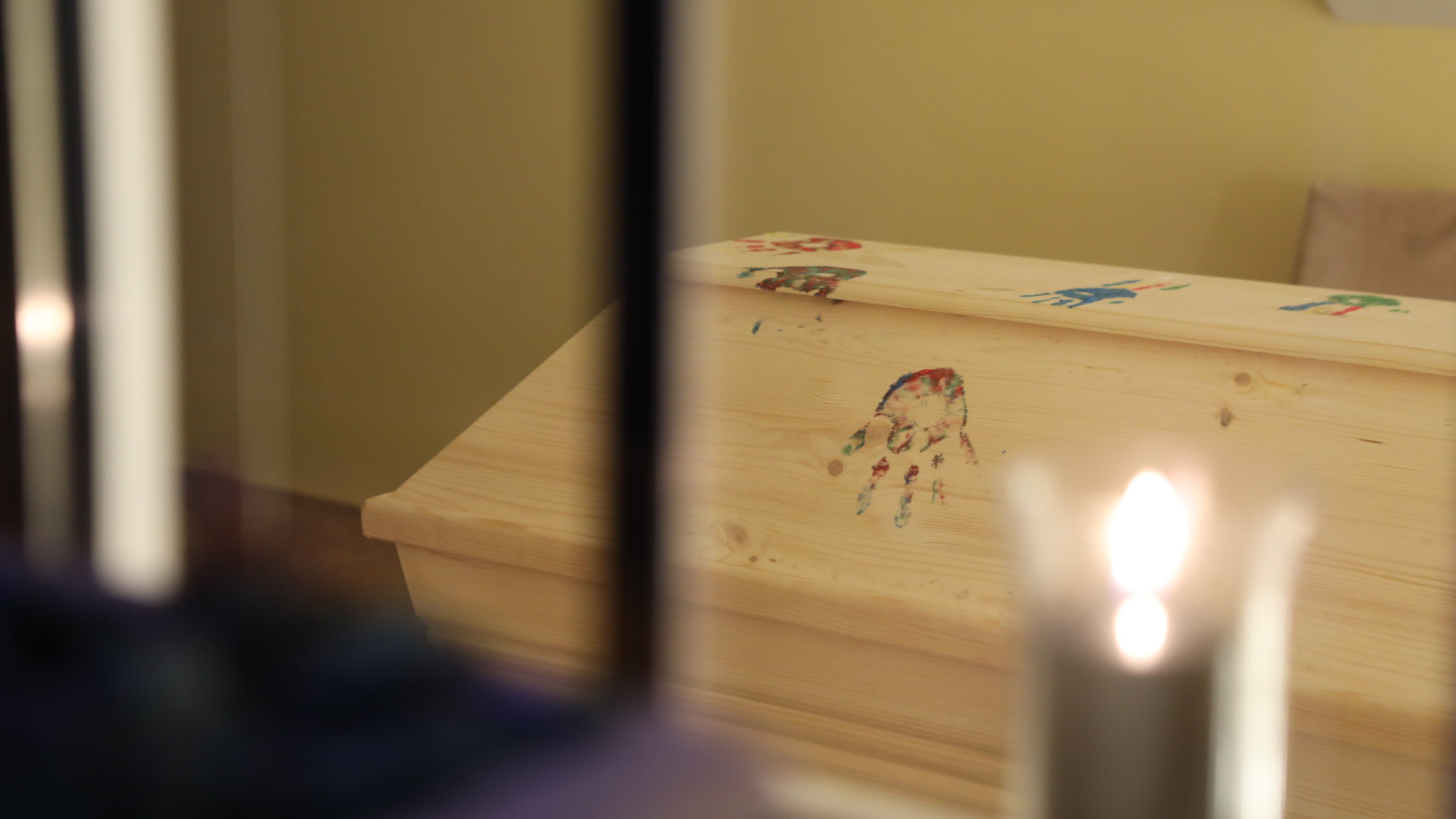 "plan b: Leben mit dem Ende - Vom anderen Umgang mit der Trauer": Ein Holzsarg ist mit bunten Handabdrücken verziert. Davor brennt eine Kerze.