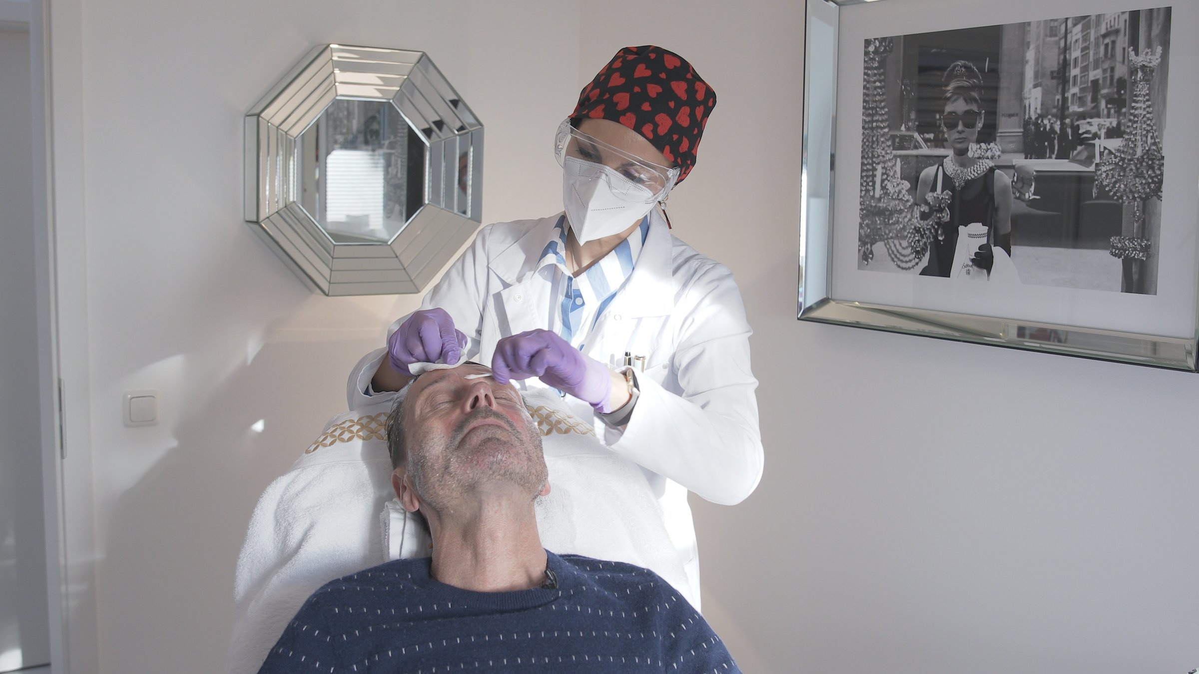 "37°: Spieglein, Spieglein an der Wand – Von Botox und anderen Versprechungen": Eine Ärztin mit Maske und Schutzbrille trägt eine Betäubungscreme auf die Stirn eines männlichen Patienten auf.
