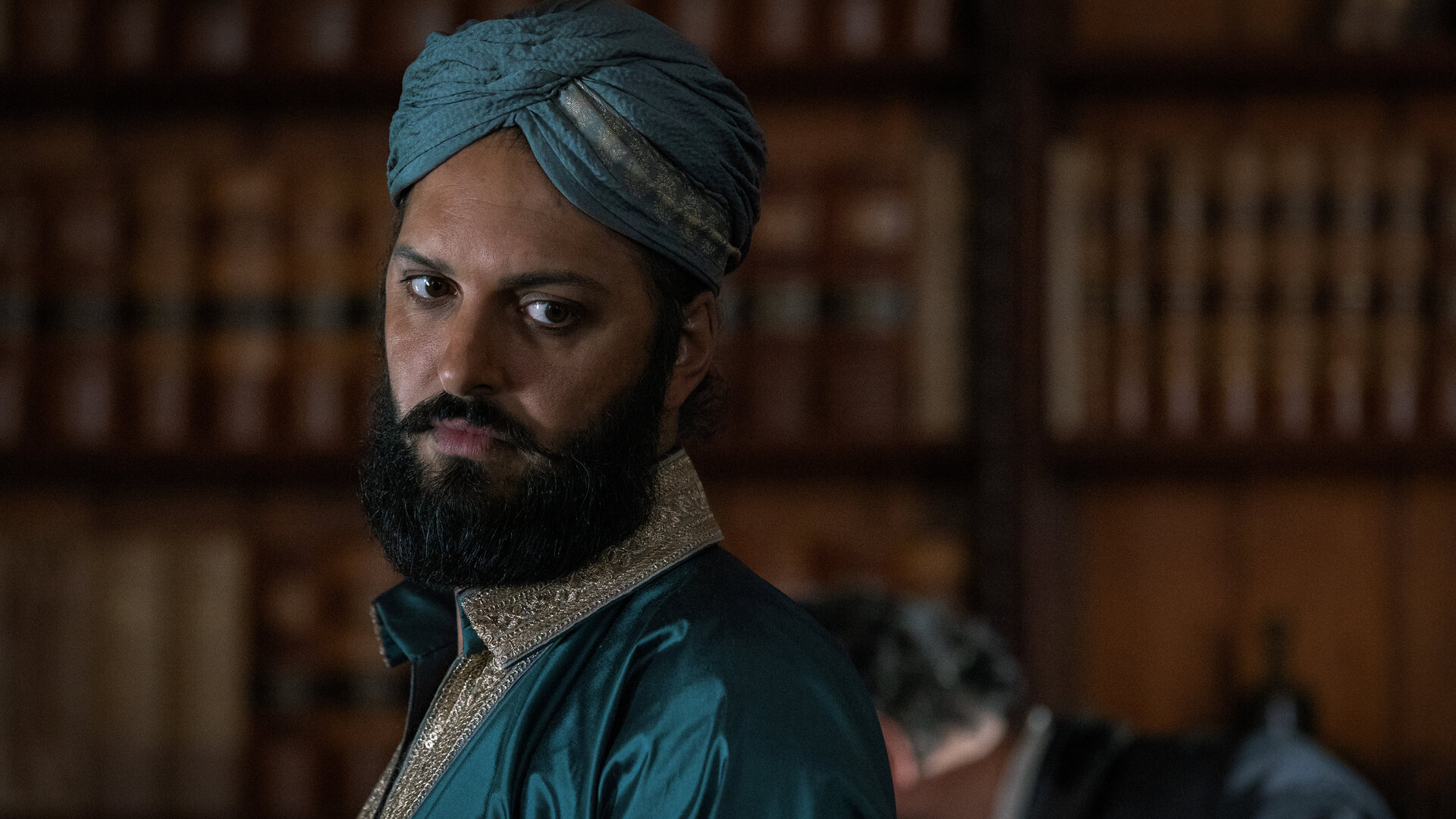 "Nautilus - Die Aktionäre": Nemo (Shazad Latif) steht in einem Raum vor einem Bücherregal. Er trägt elegante indische Kleidung und einen Dastar als Kopfbedeckung.