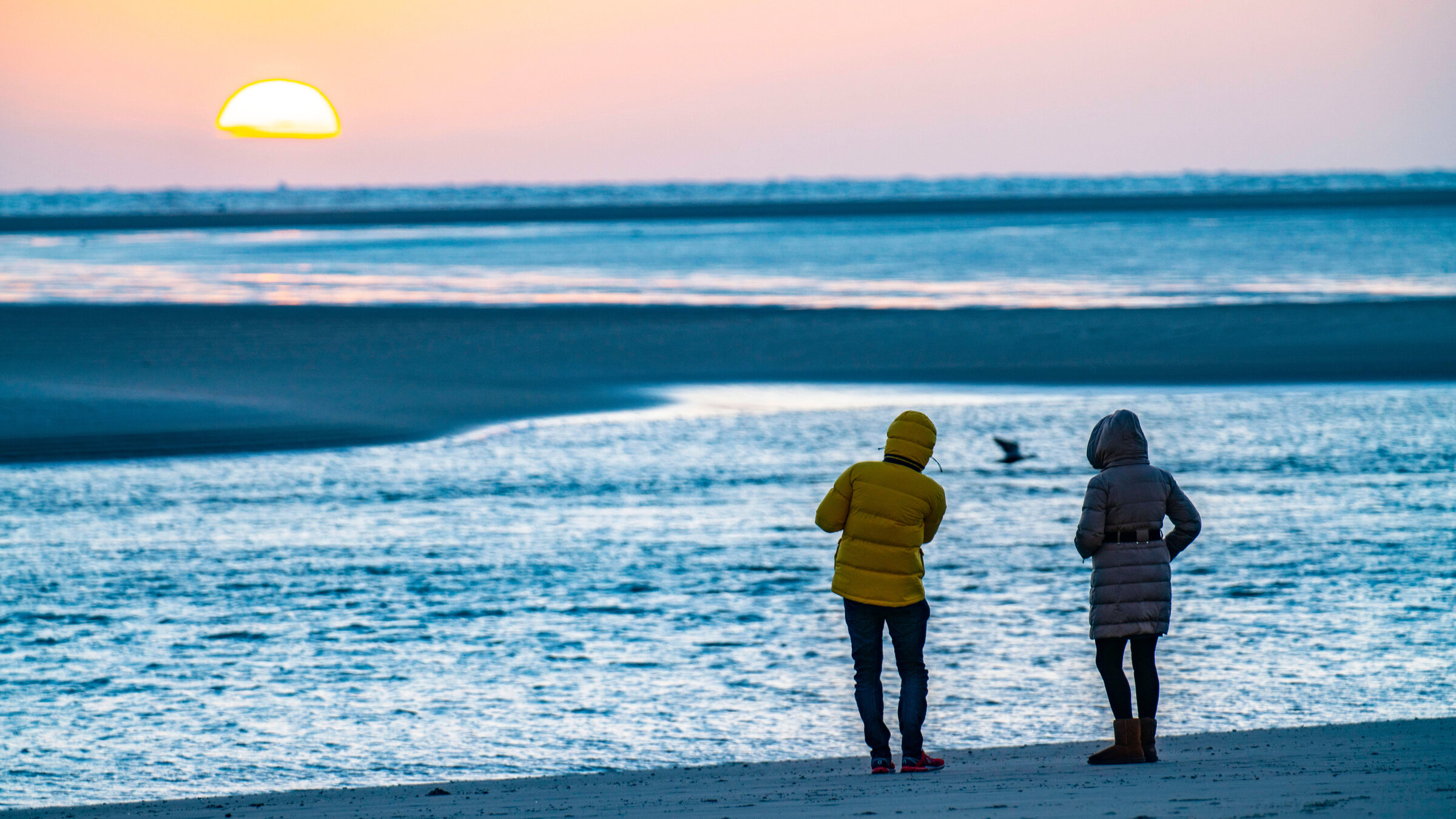 "ZDF.reportage: Borkum im Winter - Frische Brise, echtes Leben": Zwei Menschen in Winterjacken am Stand bei Sonnenuntergang
