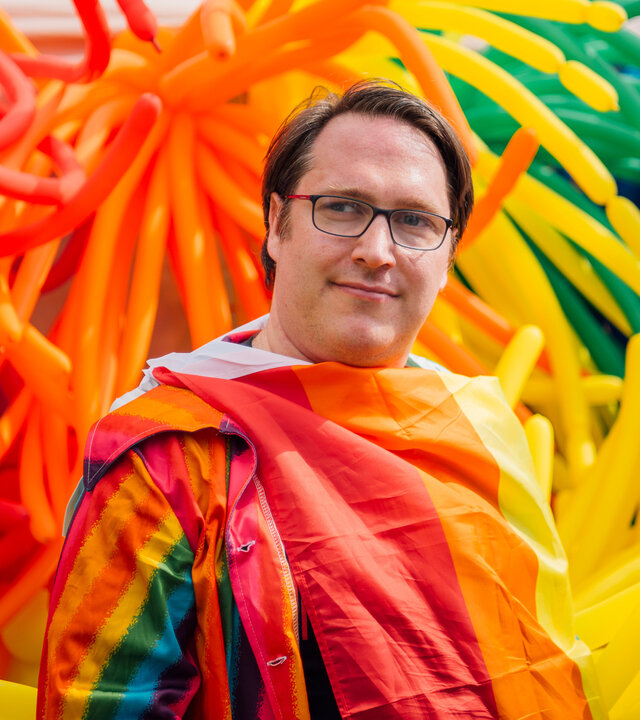 "einfach Mensch": Martin Bühren: Queer mit Behinderung" Martin Bühren auf einer Wiese mit einer Regenbogenflagge