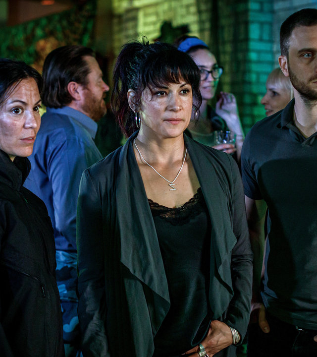 "Kommissar Beck: Rage Room": Åsa Karlsson (Johanna Lazcano), Cissi Karlsson (Malin Arvidsson) und Josef Eriksson (Martin Wallström) stehen in einer Halle für Adventure Games und blicken in eine Richtung. Hinter ihnen stehen weitere Gäste.
