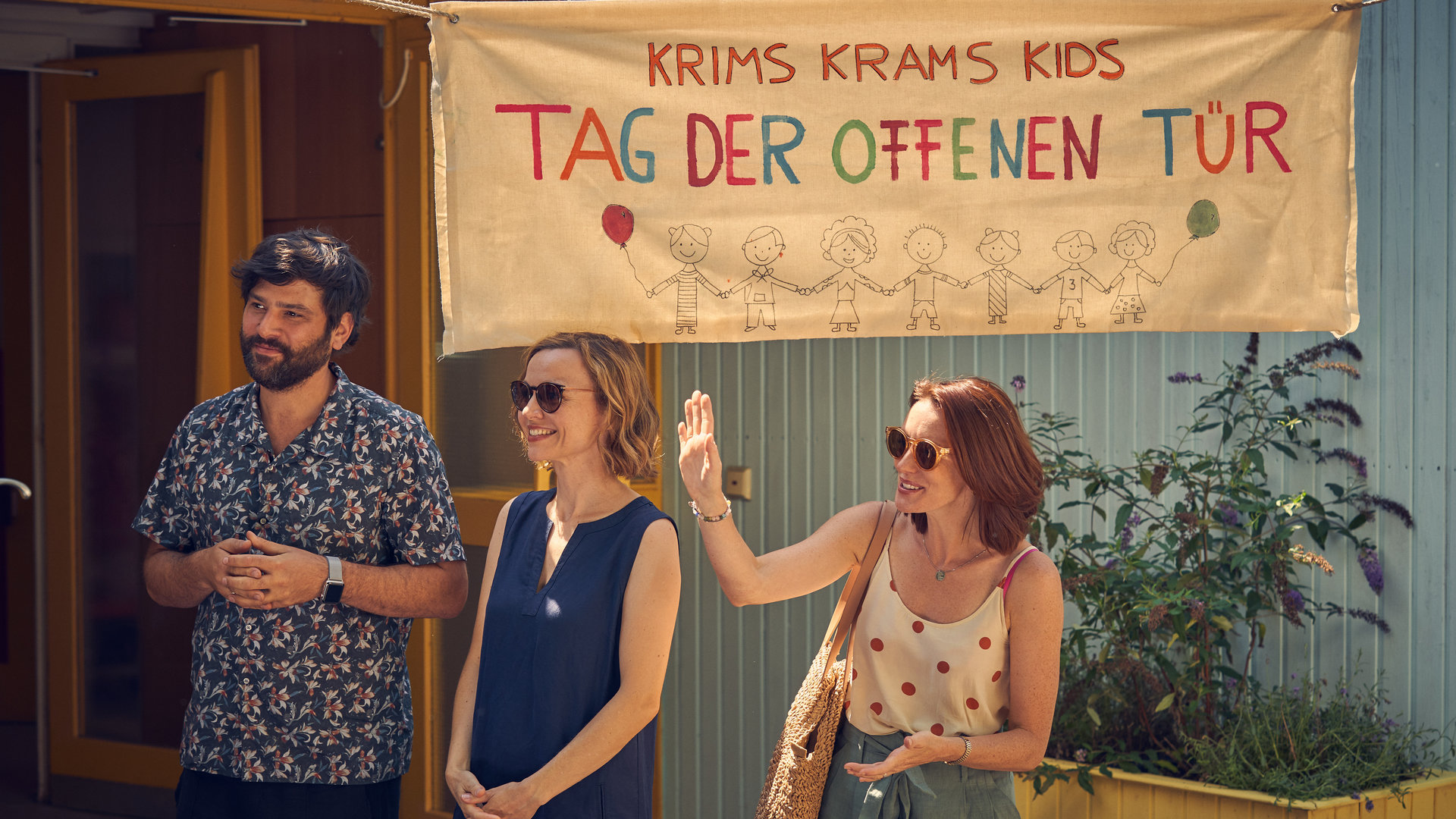 "Andere Eltern 2 – Episode 5": Jannos (Jasin Challah), Anita (Nadja Becker) und Nina (Lavinia Wilson) stehen am Tag der offenen Tür vor dem Eingang der Kita und begrüßen die Interessenten fröhlich.