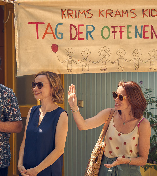 "Andere Eltern 2 – Episode 5": Jannos (Jasin Challah), Anita (Nadja Becker) und Nina (Lavinia Wilson) stehen am Tag der offenen Tür vor dem Eingang der Kita und begrüßen die Interessenten fröhlich.