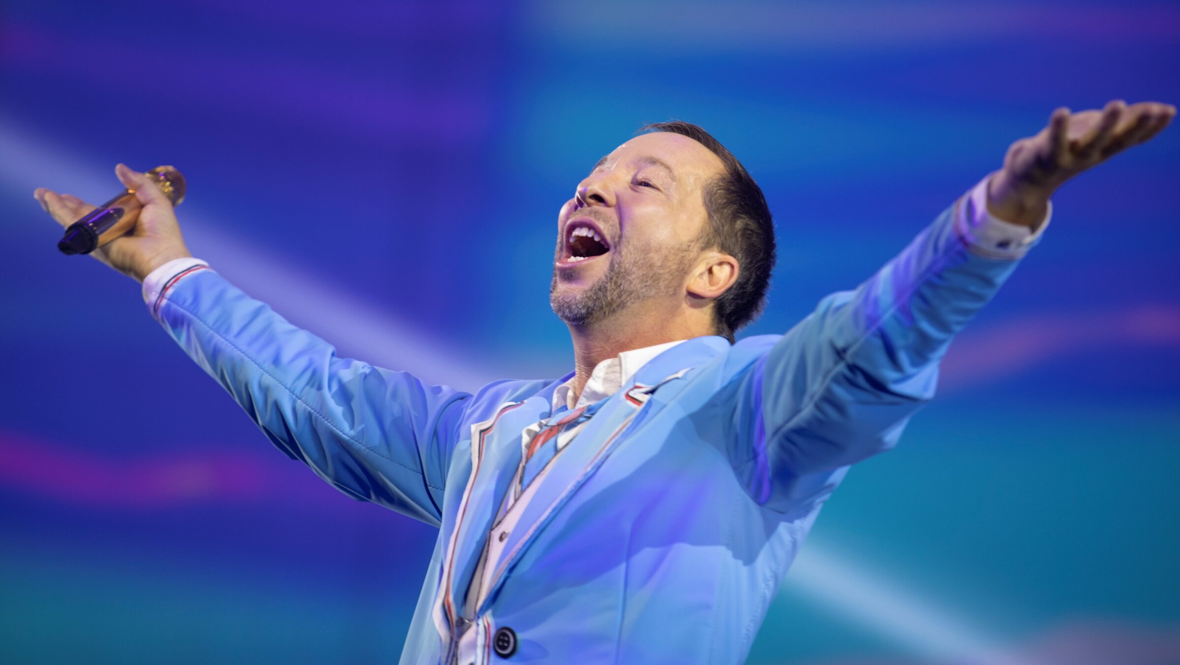 "DJ Bobo: EVOLUT30N - Live in Berlin": Nahaufnahme von DJ Bobo. Er hat die Arme zu Seite ausgestreckt und den Kopf erhoben. Bekleidet ist er mit einem hellblauen Jackett.