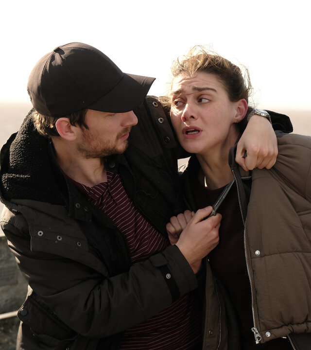 "The Killing Kind: Wolf 17": Auf einem Pier: Jake Seaton (Charles Furness) hält Ingrid (Emma Appleton) ein Messer an den Hals. Hinter ihnen verläuft eine Brüstung, dahinter liegt das Meer.