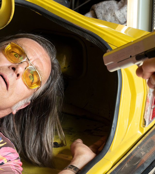 "SOKO Stuttgart – Sonnengruß ins Jenseits": Karl-Heinz Schrothmann (Michael Gaedt) liegt im Kofferraum eines Autos. Eine Person zielt mit einer Pistole drohend auf ihn, man sieht jedoch nur deren Arm. Schrotti starrt angsterfüllt in den Lauf der Waffe.