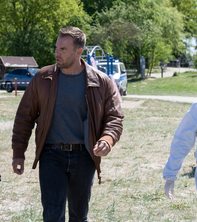 "SOKO Wismar – Der bärtige Piet": Kriminalhauptkommissarin Karoline Joost (Nike Fuhrmann) und Kriminalhauptkommissar Lars Pöhlmann (Dominic Boeer) laufen mit Kriminaltechnikerin Roswitha Prinzler (Silke Matthias) über einen Spielplatz auf den Tatort zu. Im Hintergrund arbeiten zwei Kollegen (Komparsen) der Spurensicherung.