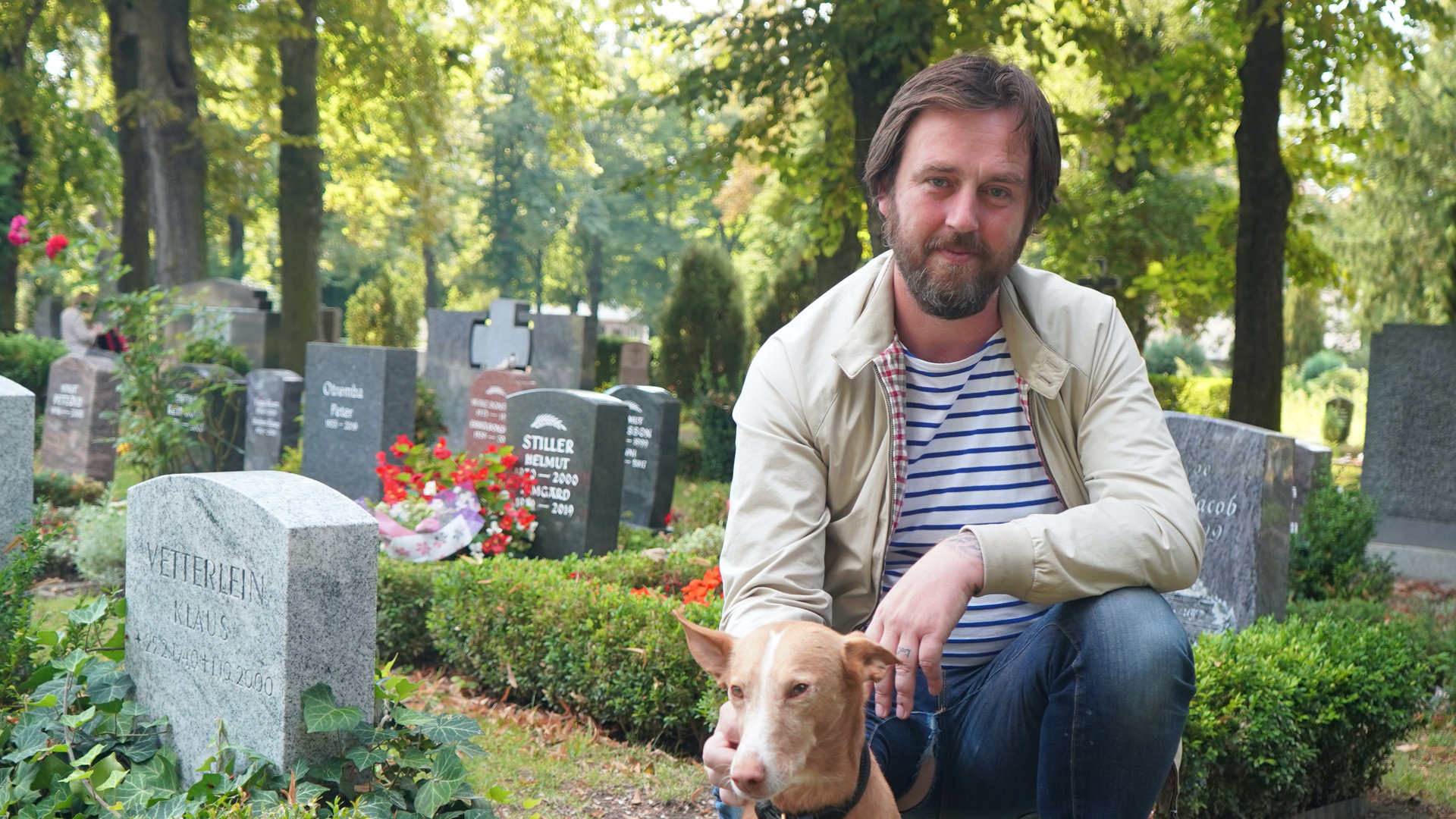 "37°: Mehr als Sarg und Service - Die neuen Bestatter*innen": Eric kniet vor Gräbern auf einem Friedhof, sein Hund sitzt neben ihm.