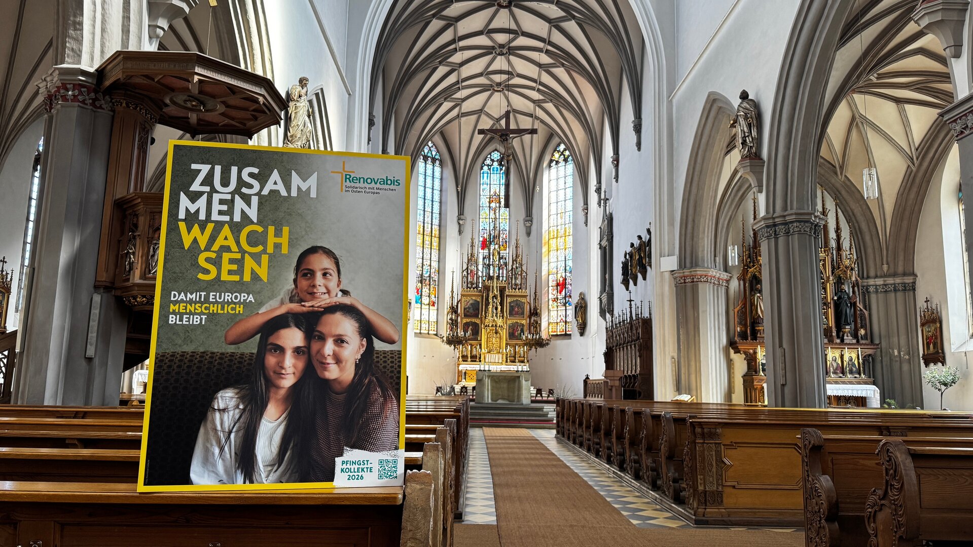 "Katholischer Pfingstgottesdienst - Zusammen wachsen für ein menschliches Europa": Innenansicht der Stadtpfarrkirche St. Martin in Kaufbeuren mit Blick zum Altar und großem Mottoplakat.