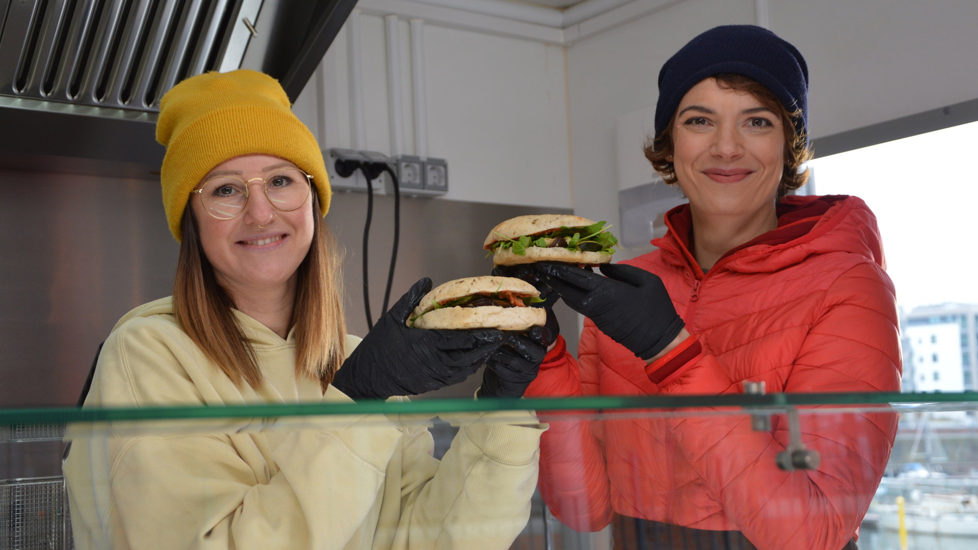 "Terra Xpress: Power im Dorf! - Energiewende von unten": Moderatorin Lena Ganschow mit einer jungen Frau im Foodtruck. Beide haben einen Burger in den Händen.