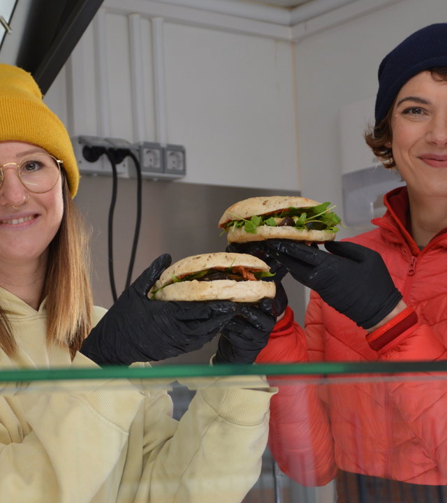 "Terra Xpress: Power im Dorf! - Energiewende von unten": Moderatorin Lena Ganschow mit einer jungen Frau im Foodtruck. Beide haben einen Burger in den Händen.