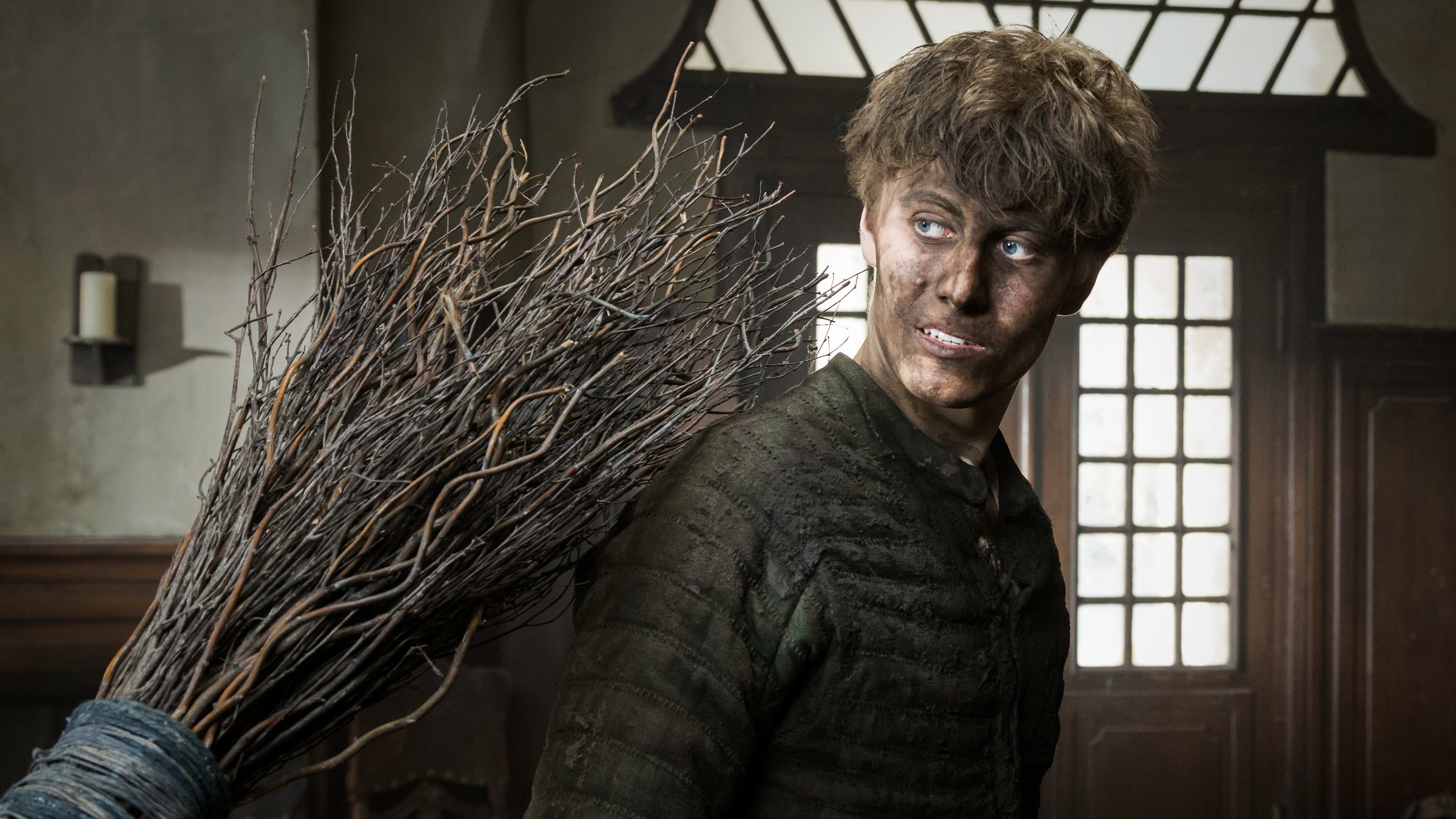 "Der Zauberlehrling": Im Inneren der Apotheke steht Valentin (Max Schimmelpfennig) mit von Dreck schwarzem Gesicht und gekleidet in einen wattierten, dunkelgrünen Wams. Mit großen Augen dreht er sich einem Reisigbesen zu, der Valentin auf die Schulter schlägt.