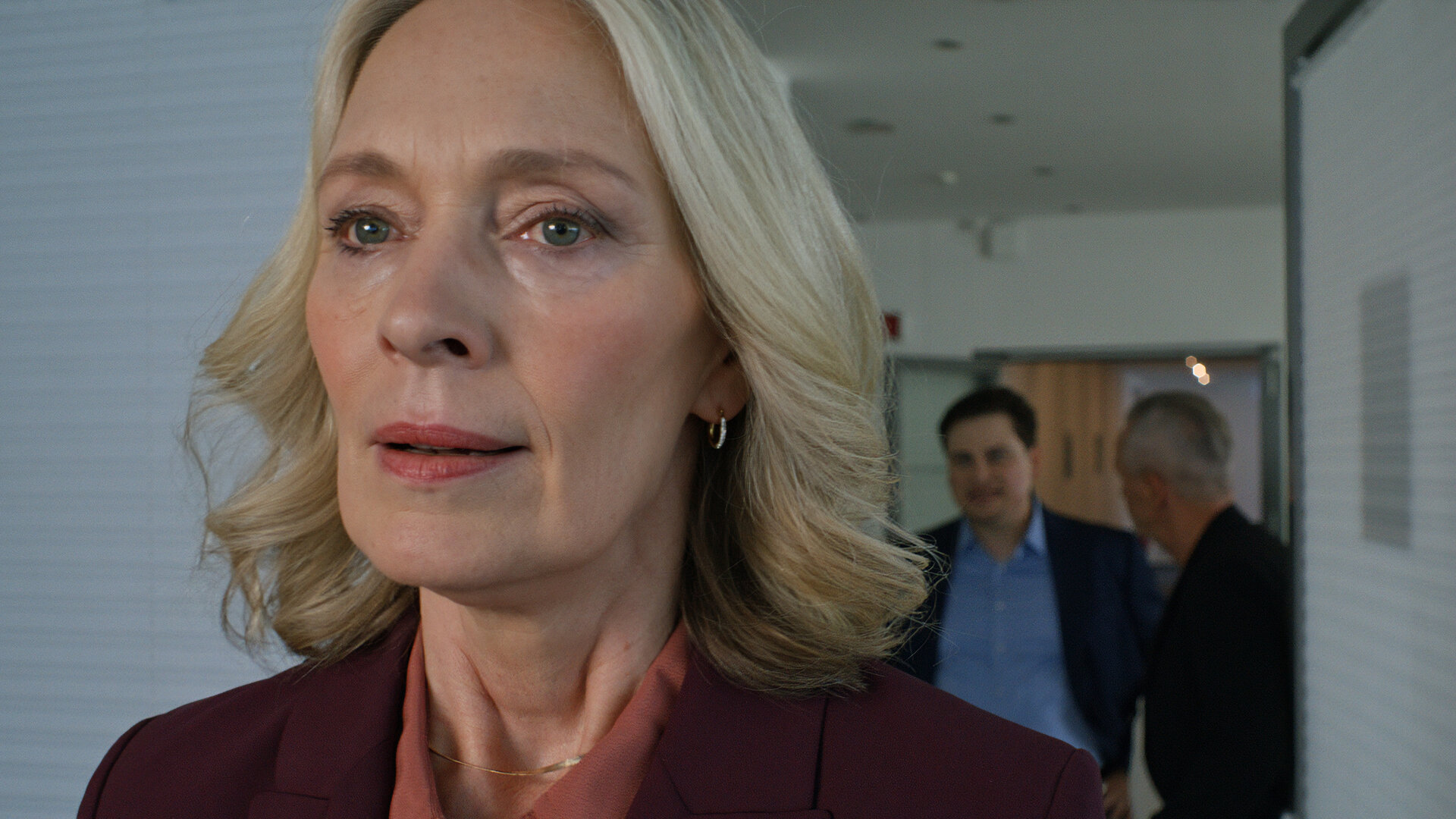 "Notruf Hafenkante - The show must go on": Großaufnahme von Karin Sievers (Katja Weitzenböck) im Vordergrund. Sie blickt nachdenklich ins Leere. Im Hintergrund verschwommen stehen Gunnar Bremer (Claudiu Mark Draghici) und Oliver Meixner (Tim Wilde).