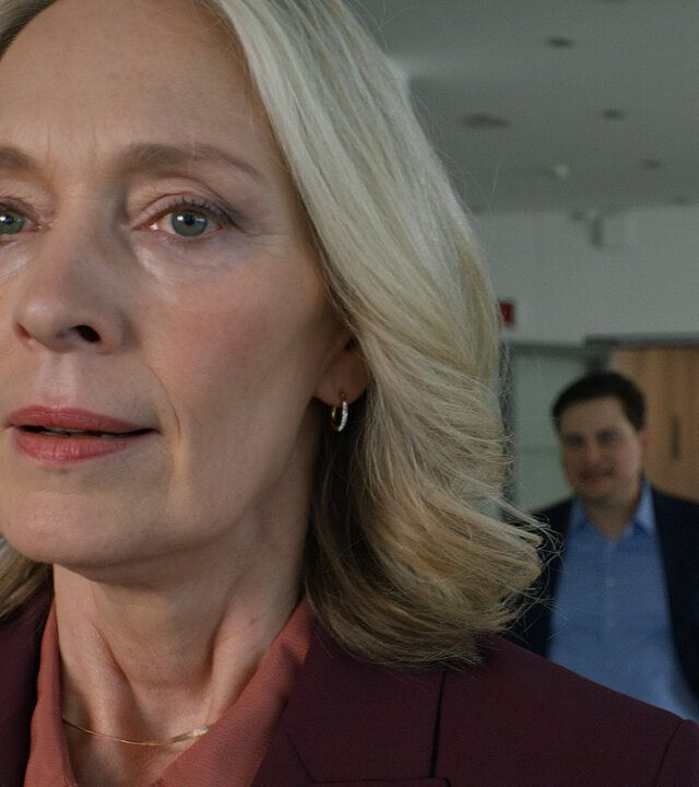 "Notruf Hafenkante - The show must go on": Großaufnahme von Karin Sievers (Katja Weitzenböck) im Vordergrund. Sie blickt nachdenklich ins Leere. Im Hintergrund verschwommen stehen Gunnar Bremer (Claudiu Mark Draghici) und Oliver Meixner (Tim Wilde).