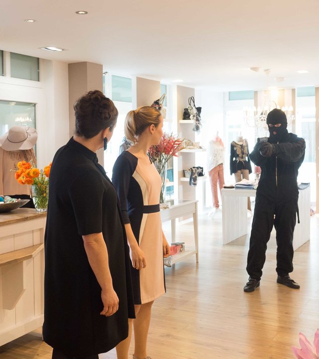 "SOKO Wismar – Das Fenster zum Hof“: Im Modeladen stehen Besitzerin Carla Ritter (Gabriele Völsch), ihre Angestellte Jessy Dietz (Mira Elisa Goeres) und die Kundin Hanne Söderbaum (Anja Karmanski) nebeneinander und schauen in Richtung des maskierten Mannes. Dieser richtet eine Waffe auf sie.