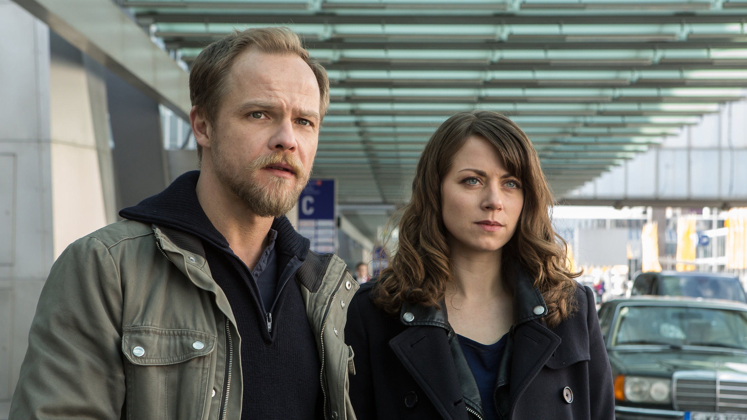 "Kommissar Marthaler- Die Sterntaler-Verschwörung": Kommissar Marthaler (Matthias Koeberlin) und seine neue Kollegin Sarah (Alice Dwyer) stehen vor der Ankunftshalle des Frankfurter Flughafens.