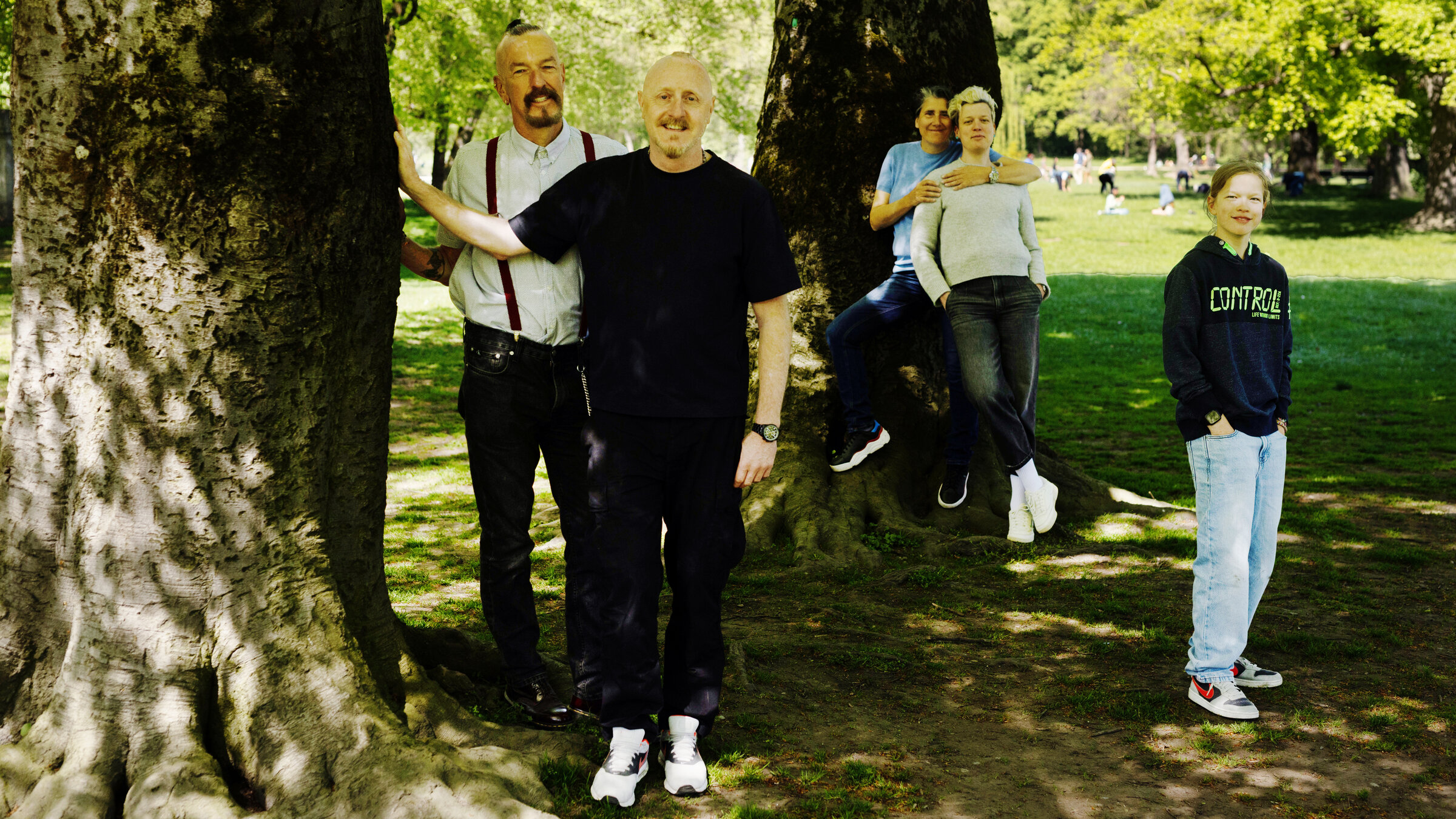 "37°: Meine ziemlich bunte Familie": Links neben einem großen Baum im Englischen Garten in München stehen Herbert und Christian, dahinter, vor einem anderen großen Baum Andrea, die Judith umarmt. Rechts daneben steht Oskar. Alle blicken in die Kamera.